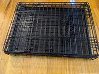 Top-down view of folded black metal dog crate showing wire mesh construction and plastic base tray beneath.