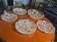 Photo of five clear glass bowls and plates with star and geometric cut patterns on wooden table, near mint condition.
