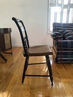 Side view of one black painted Hitchcock chair with natural wood seat showing turned legs and spindle backrest.