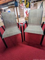 Front view of two lawn chairs side by side on red carpet with visible metal armrests and mesh fabric seating, showing signs of use.