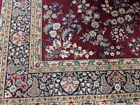 Close-up photo showing floral and paisley detailed border design of the rug with colors red, blue, cream, and beige.