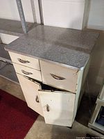 Front angled view of a Mid Century Modern metal tool cabinet showing the textured gray metal top, two drawers and two cabinet doors, one door ajar.