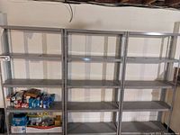 Front view of three metal storage shelves connected side by side with some boxes and small items on lower shelves.