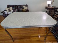 View of the mid-century modern kitchen table showing the top surface and metal legs on a wooden floor in front of a couch.