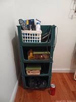 Green plastic stacking shelving unit with four shelves, filled with various household items for scale. A soda can is placed next to the unit for size reference.