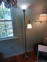 Photo of a brass floor lamp with two frosted glass lampshades by a window in a room.
