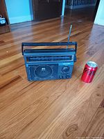 Front view of Panasonic portable radio with soda can for size reference on wooden floor.