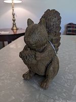 Front angled view of wooden squirrel figurine sitting upright holding an acorn with textured tail visible.