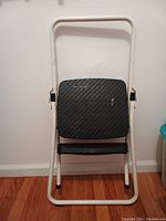 Front view of white metal folding step stool with two black steps, folded upright.