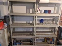 Front view of two beige plastic storage shelves against a wall with assorted items on the shelves.