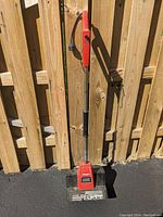 Full front view of the Toro electric handheld snow shovel resting against a wooden fence on a paved surface under sunlight.