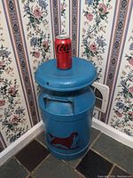 Milk can positioned in corner against floral wallpaper, showing top and side with dog silhouette.