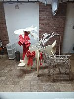Photo showing a silver wire framed reindeer Christmas decoration with integrated string lights and red bows tied around the neck. Displayed on a tiled floor in a room with brick wall background.