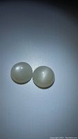 Photo of two natural white moonstone round cabochon gemstones with visible flash under direct lighting.