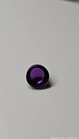 Close-up image of the single round cabochon amethyst gemstone showing deep purple color and polished smooth surface.