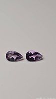 Pair of pear cut purple amethyst gemstones in close-up, showing shape, color and clarity on white background.