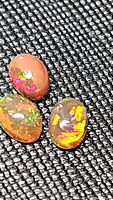 Close-up of three oval chocolate opal cabochons showing rainbow play of color on a black textured background.