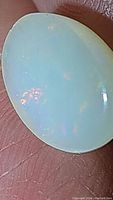 Close-up photo of oval cabochon Ethiopian opal showing translucent white base with multicolored flashes.