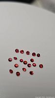 Twenty small round faceted orange-red sapphires laid on a white background showcasing size, shape, and clarity.