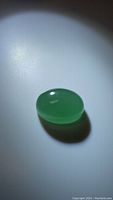 Top view of a smooth oval cabochon green aventurine gemstone on a white background, showing glossy polished surface and green color.