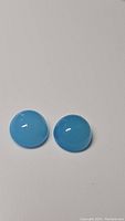 Pair of round cabochon icy blue chalcedony gemstones shown on white background, capturing their shape and color.