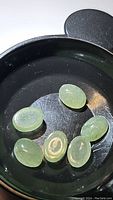 Seven mint green oval cabochon kyanite gemstones displayed in a black container showing inclusions and polish.