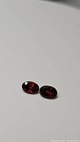 Two natural oval cut garnet gemstones from Mozambique placed side by side on a white surface, showing their deep red color and matched appearance.