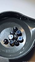 Overhead image showing 11 polished round black onyx cabochon stones placed inside a black container, showcasing their smooth, glossy surface and deep black color.