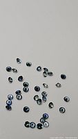 Lot of small natural blue sapphires, round cut, scattered on white background displaying vibrant deep blue hues and diamond faceting cut.