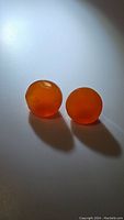 Two round mandarin orange carnelian gemstones placed side by side under direct lighting, showing rich orange color and smooth polished surface.