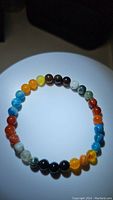 Top view of a multicolored natural gemstone bead bracelet featuring blue, yellow, red, black, and green agate beads, laid flat in a circular arrangement.
