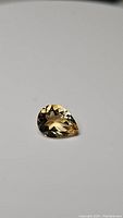 Single pear cut natural golden citrine gemstone with high luster photographed on white background.