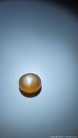 Photo showing natural round peach moonstone cabochon with smooth surface on a light background under direct light to highlight color and flash.