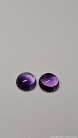 Two round cabochon purple amethyst gemstones displayed on a flat surface