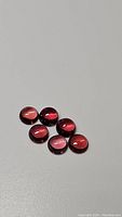 Six round cabochon garnet gemstones grouped on a neutral gray background, showing their pink to orange coloration.