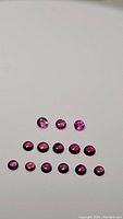 Photo showing 3 bright round cut pink sapphires and 11 round cabochon deep red pink sapphires arranged on white background
