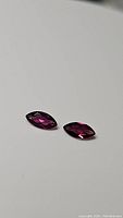 Pair of marquise cut purple-pink rhodolite garnet gemstones on white background showing their size and color.