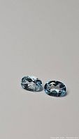 Pair of oval cut natural sky blue topaz gemstones shown on a plain background with good lighting to capture color and faceting details.
