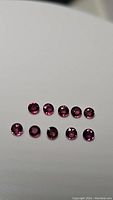 Photo of 10 round cut purplish-pink sapphires arranged in two rows showing size and uniformity.