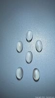Top down view of six oval-shaped cabochon white moonstone gemstones arranged in a circle on a flat surface.