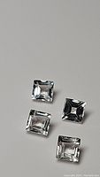 Four natural square cut white topaz gemstones on a neutral background, showing clarity and cut.