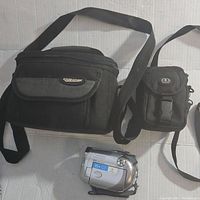 Canon DC230 DVD camcorder front view with accessories including a larger Case Logic carrying case and a smaller black camera case visible.