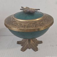Side angle view showing teal enameled body and decorative brass footed base.