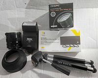 Photo of assorted camera accessories including flash, lenses, filter set, lens hood, tripod, and viewfinder attachment on a white background.
