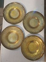 Top view of the set of four round brass coasters laid out on a white surface, showing the ornate floral and patterned engravings on each.