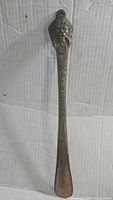 Full length photo of vintage bronze shoe horn with lion head handle on a corrugated cardboard background, showing detailed ornamental shaft and spooned end.