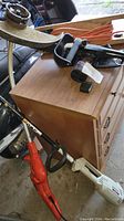 Black and Decker Grass Hog electric edger, red electric saw, and orange extension cord laid on a wooden cabinet in a garage-like environment.