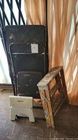 Photo showing four step ladder and stool items: large black Cosco step ladder, small black folding stool, small white plastic step stool, and wooden step ladder with metal hinges, all showing signs of use.