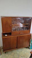 Front view of the full mid-century modern china cabinet showing wood finish, glass display area, left wood cabinet door, and lower sliding doors storage.