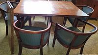 Overall view of walnut dining table with six green upholstered barrel-back chairs
